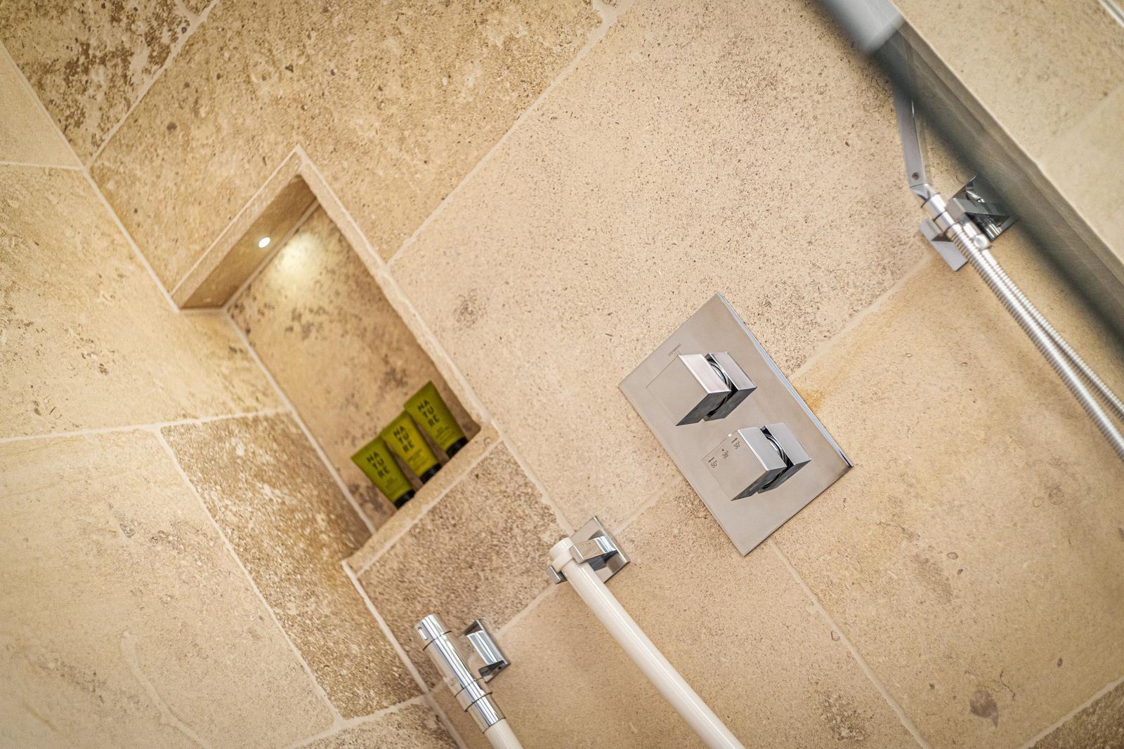 Dusche mit Steinwand, Duschbrause und integriertem Regal mit Duschgels.