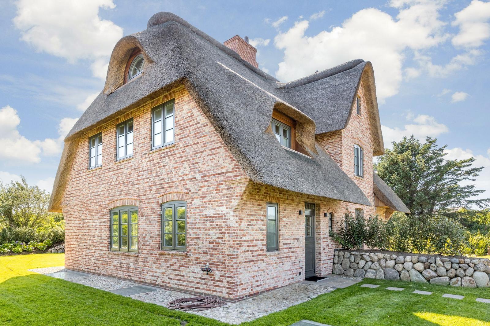 Ein zweistöckiges Haus mit strohgedecktem Dach und roten Ziegelsteinen.