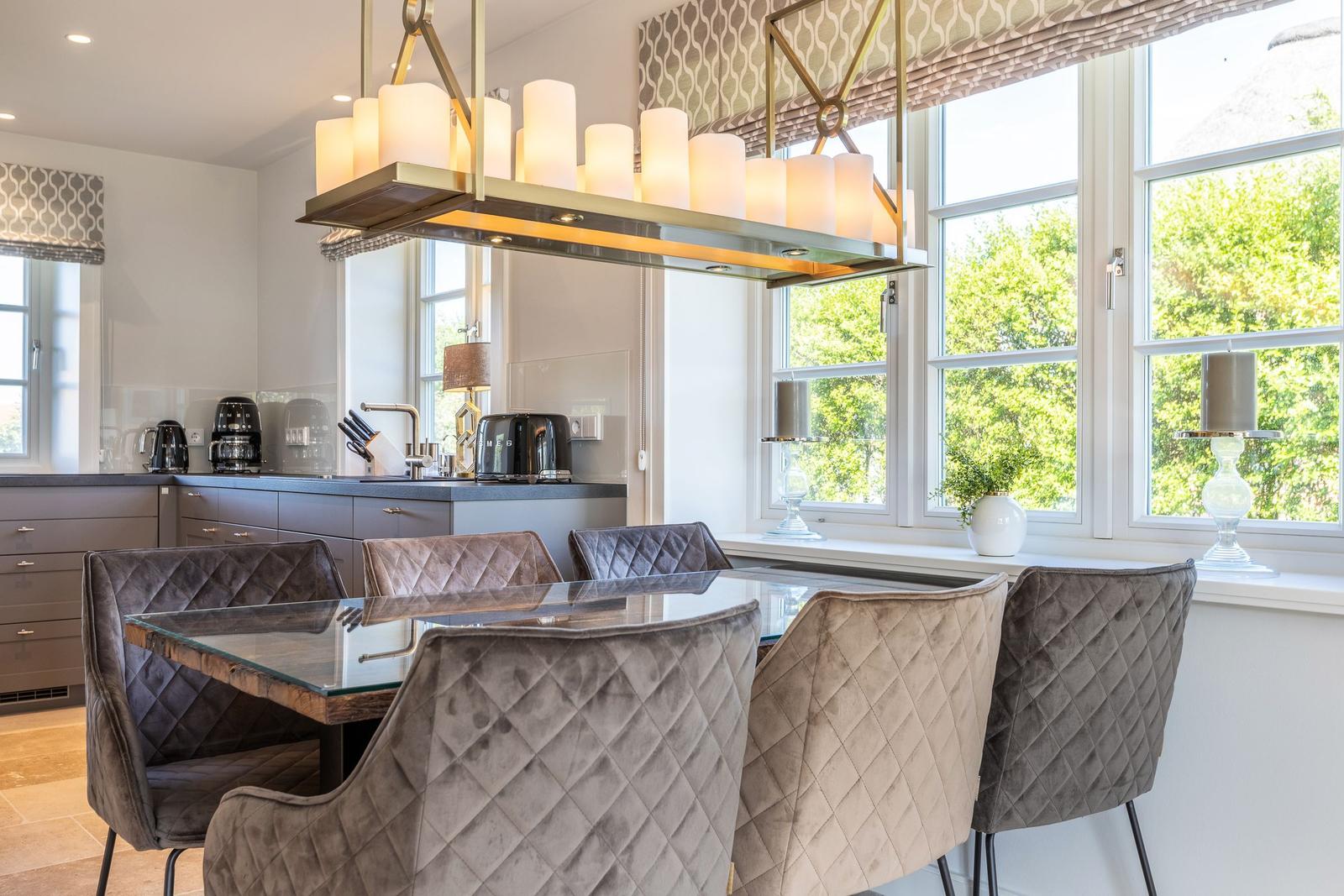 Esszimmer mit Glas-Tisch, Polsterstühlen und moderner Deckenleuchte. Große Fenster mit Blick auf Grün.