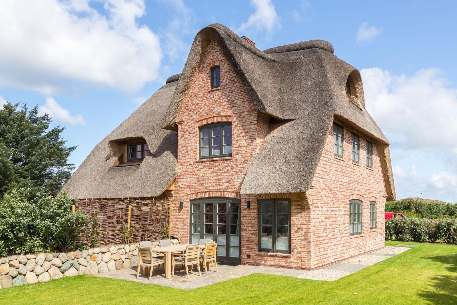 Haus mit strohgedecktem Dach und Holzterrasse im Garten