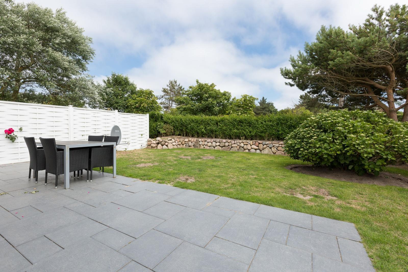 Terrasse mit Tisch und Stühlen, Grasfläche und Hinterhof mit Hecke und Steinmauer.