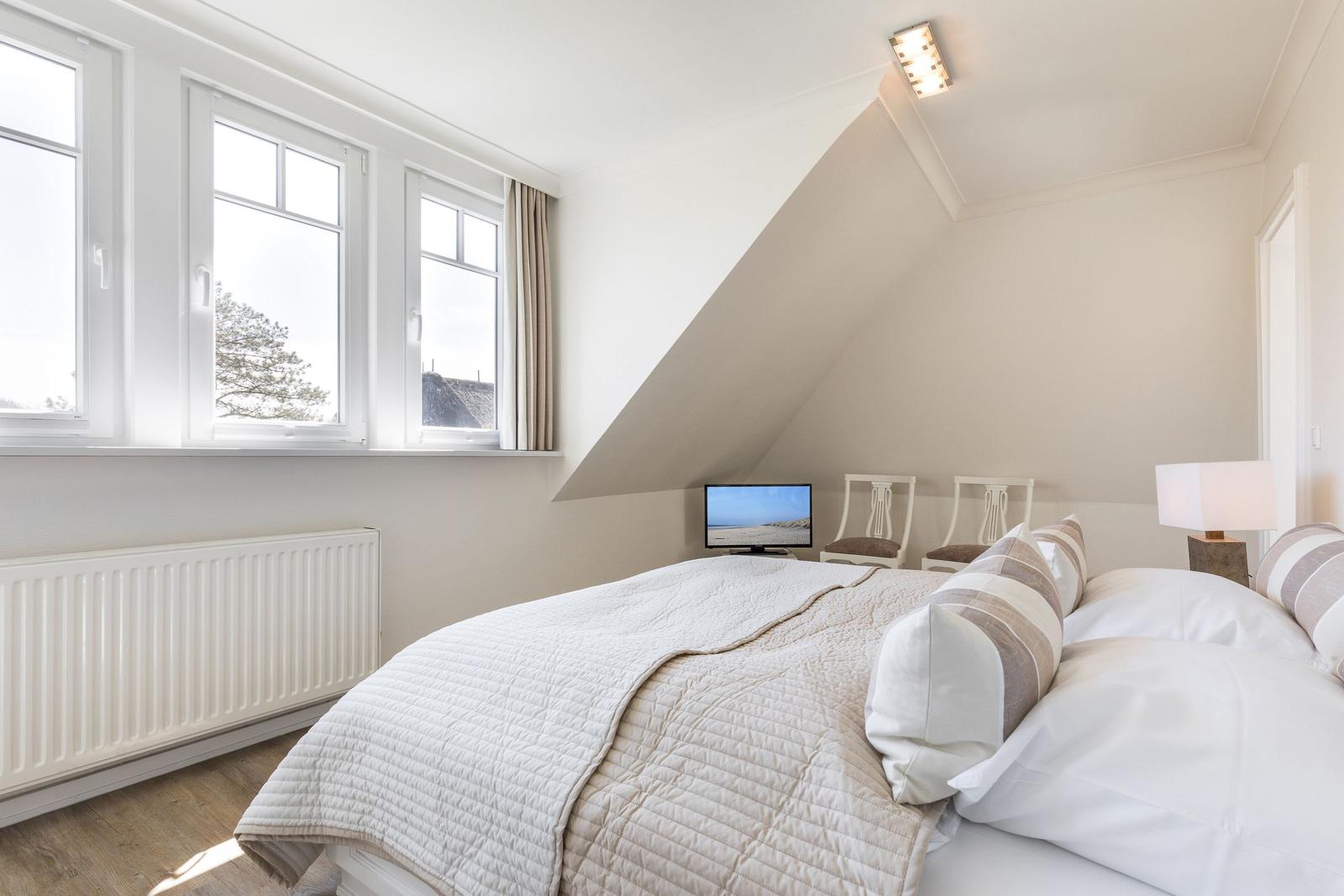 Schlafzimmer mit Dachschrägen, Fenster, Bett und Fernseher.