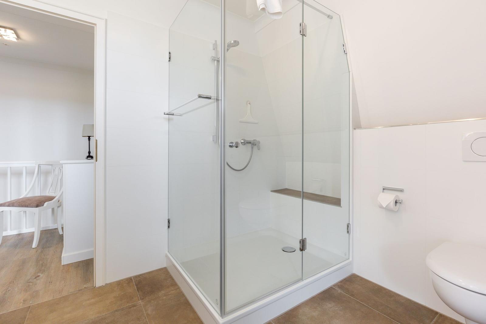 Dusche mit Glaswand, Toilette und Tür zum angrenzenden Raum.