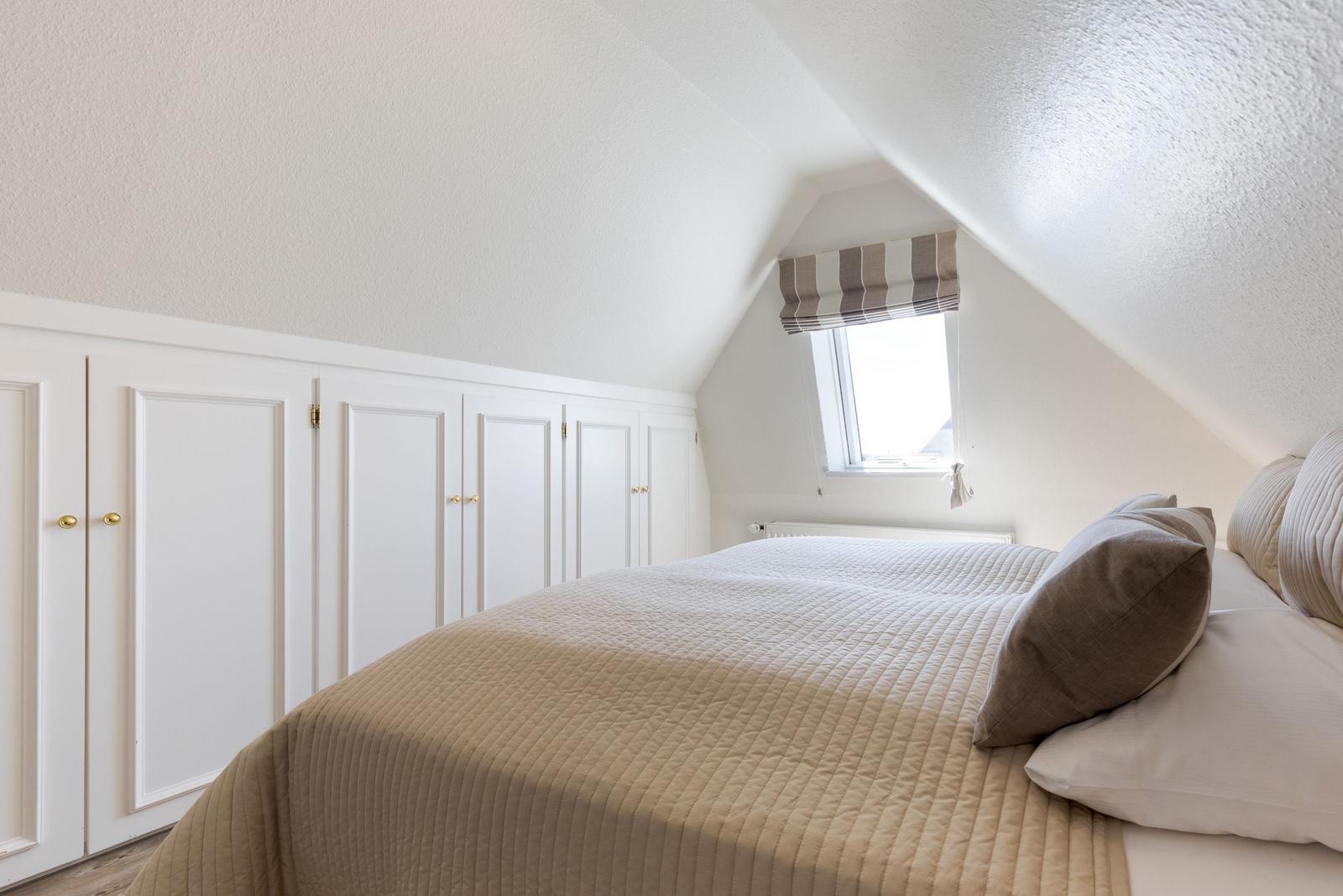 Schlafzimmer mit Dachschräge, Bett und Fenster mit Rollladen.