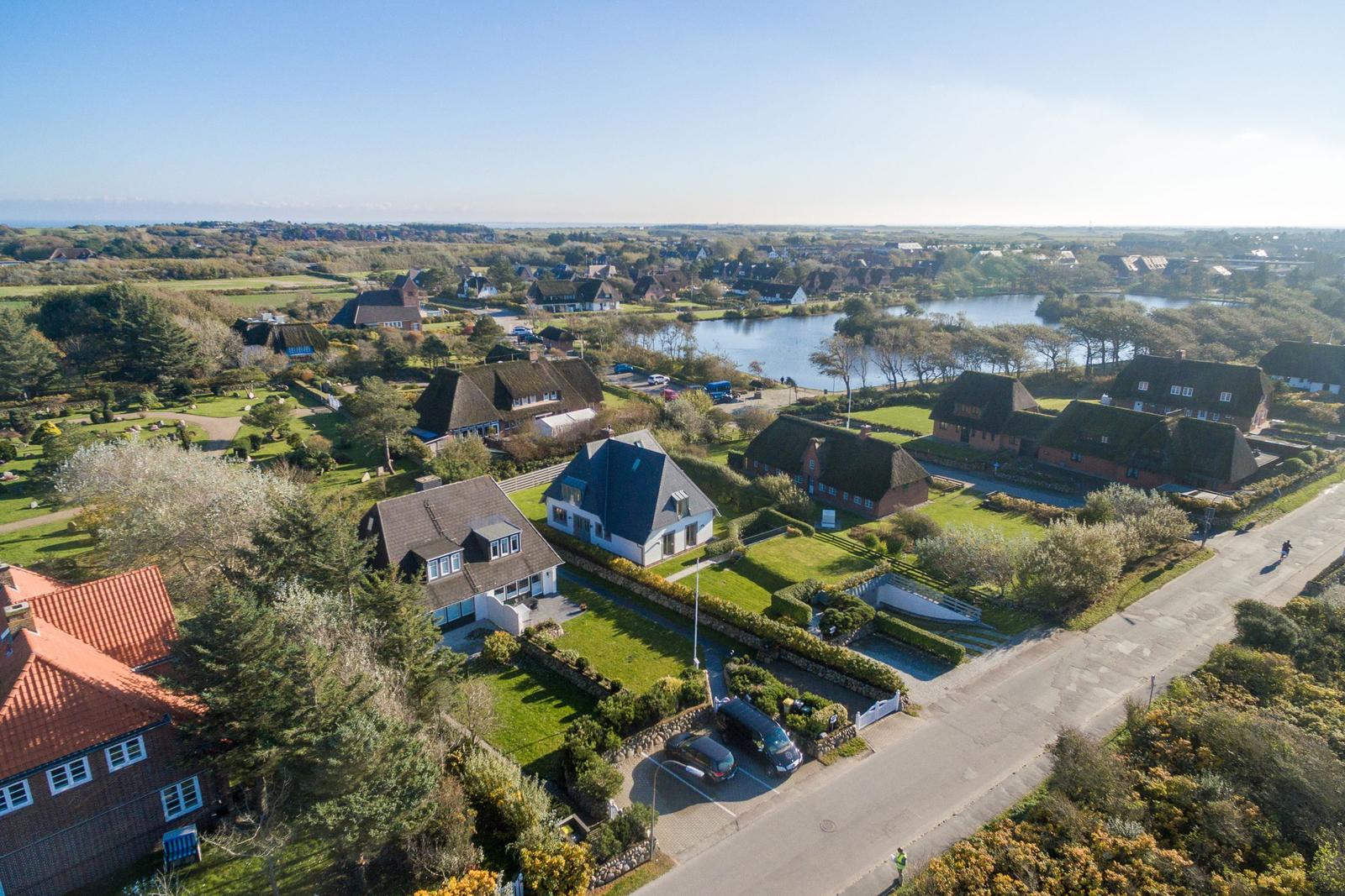 Aerial view of a village with houses, gardens, and a lake.