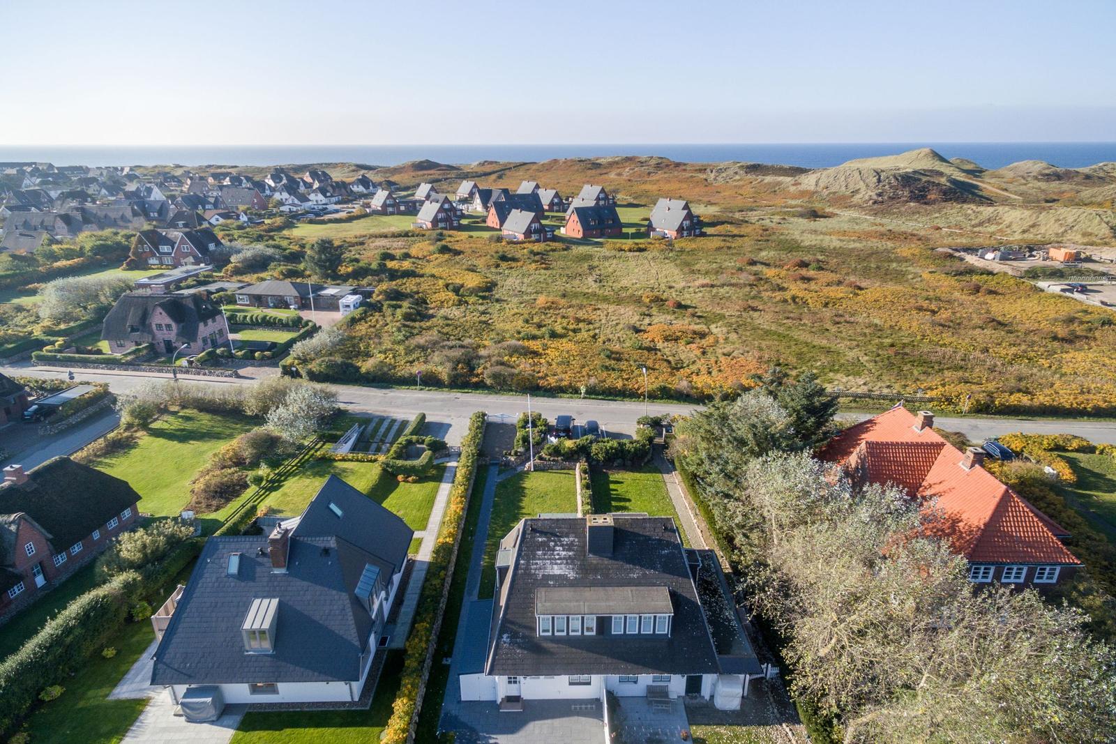 Aerial view of coastal village with houses and greenery near the sea.