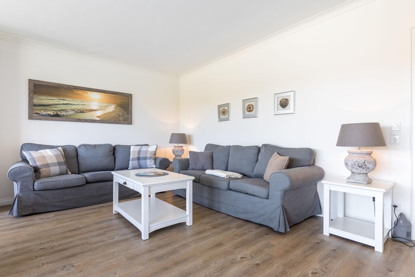 Wohnzimmer mit grauen Sofas, weißem Tisch und Holzboden.