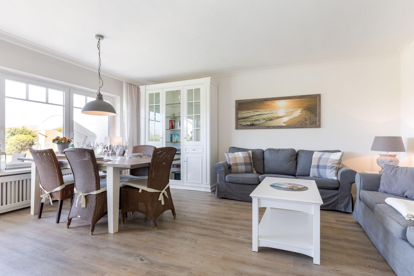 Wohn- und Essbereich mit Sofa, Tisch und Stühlen. Wandbild und Bücherregal sichtbar.