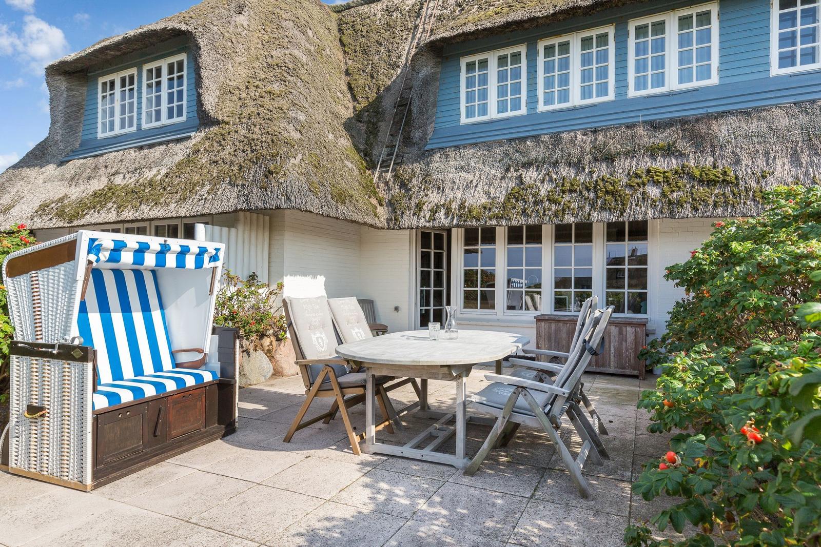 Terrace with beach chair, table and chairs in front of a house with thatched roof.