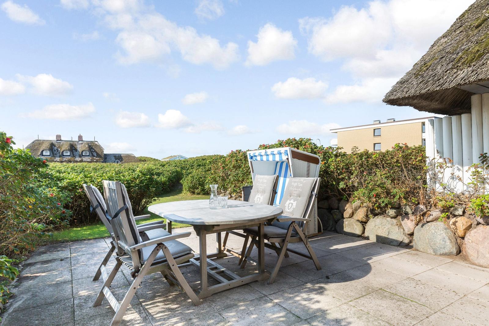 Terrace with table, chairs, and beach chairs. View of green hedge and rooftops.