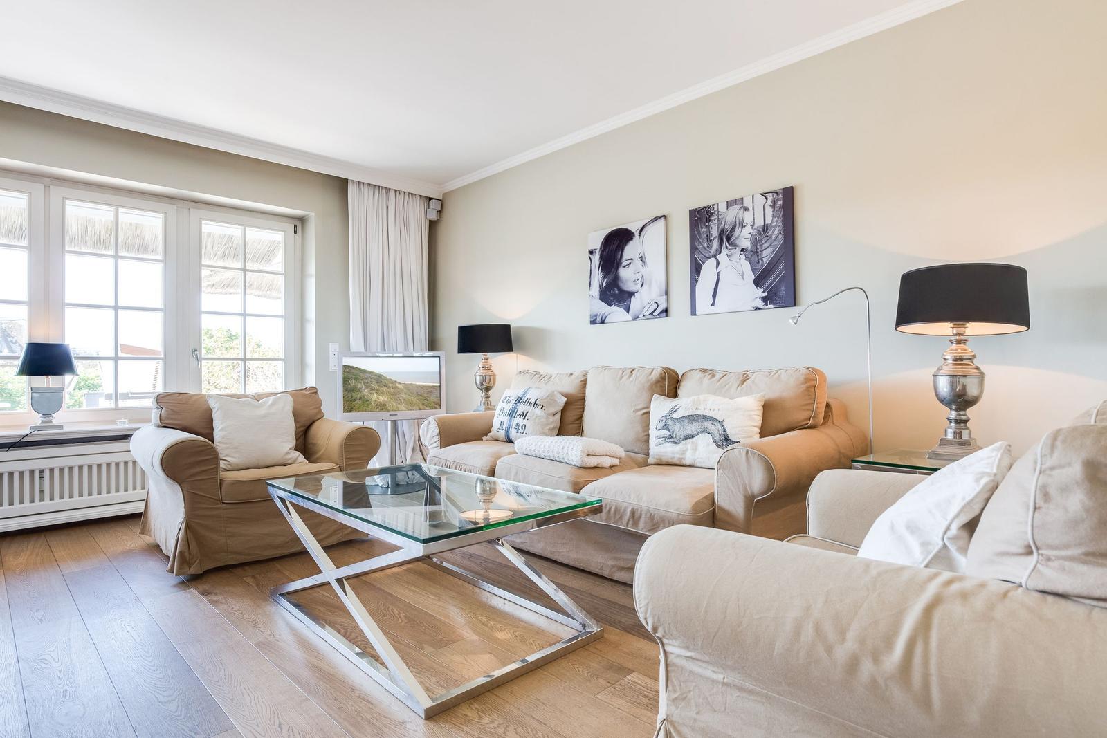 Living room with sofa, armchairs, and glass coffee table. Two pictures hang on the wall.