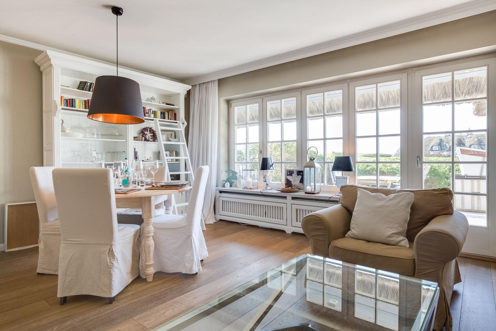 Dining area with table and chairs, living area with sofa and glass table, large windows with view outside.