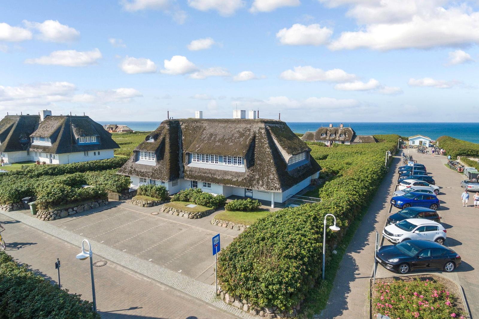 House with thatched roof, parking lot, and sea view.
