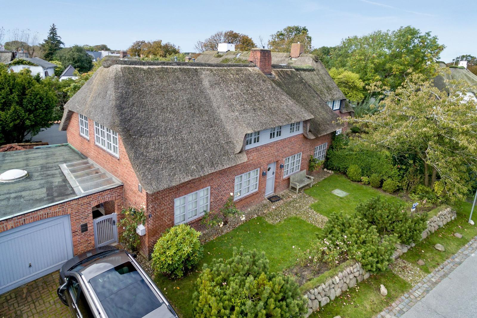 Red brick house with thatched roof, garden, and garage.