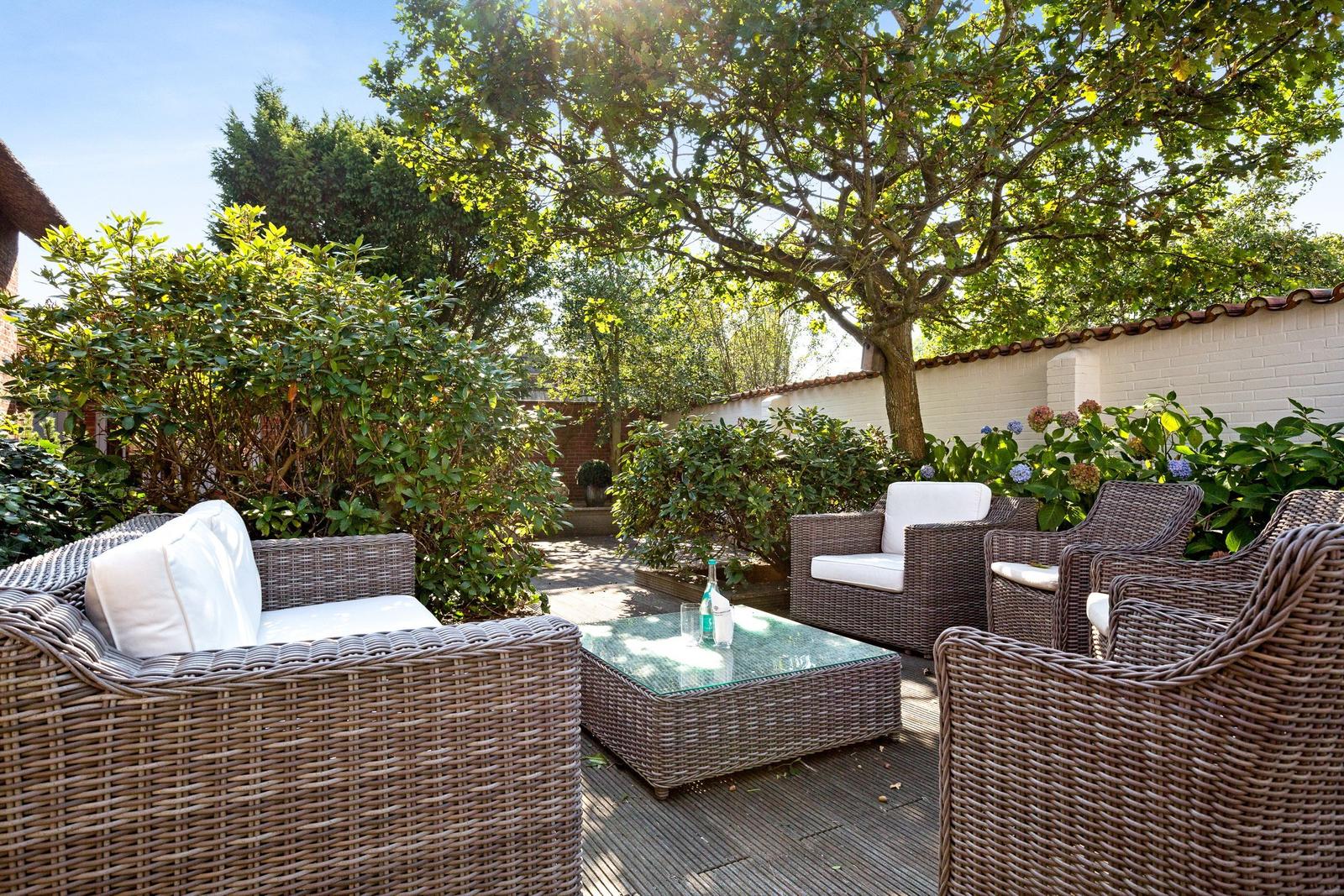 Terrace with wicker furniture and glass table under trees.