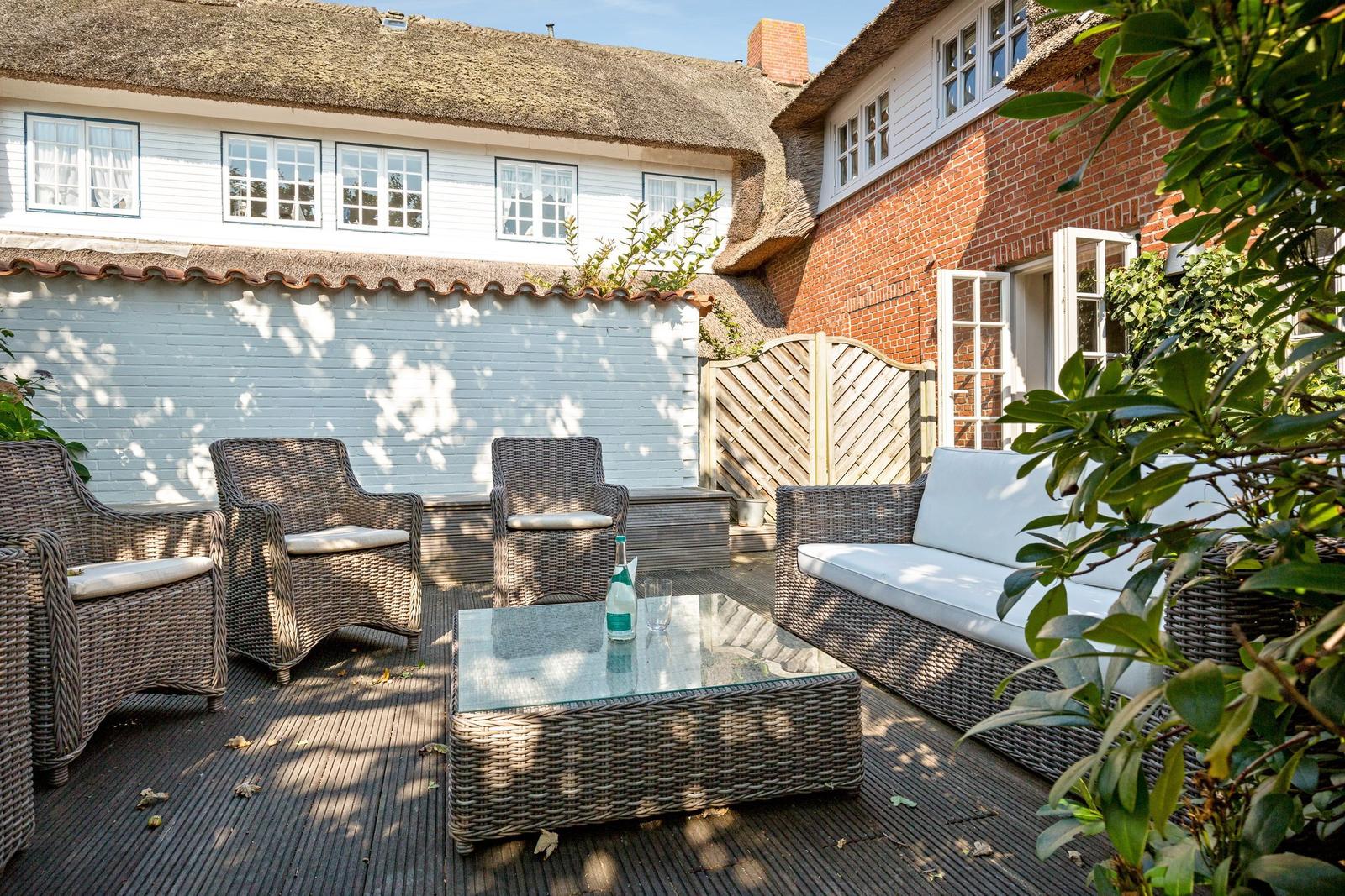 Terrace with wicker furniture and glass table in front of a thatched house.