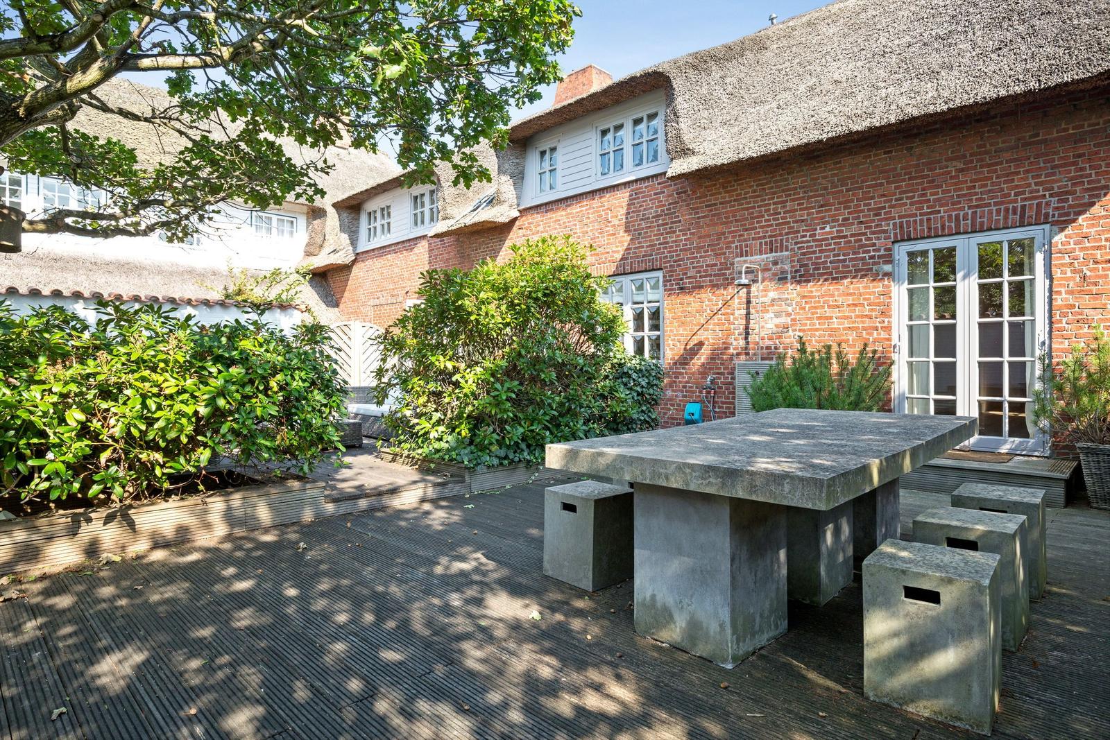 Backyard with stone bench, terrace, and red brick house with thatched roof.