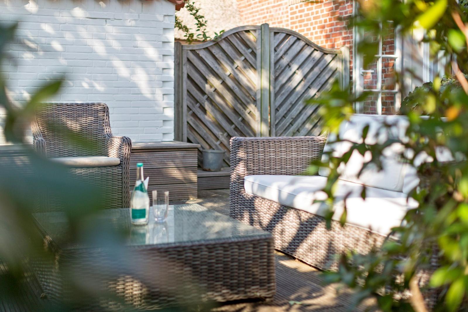 Terrace with wicker furniture, glass table, and bottle in sunlight.