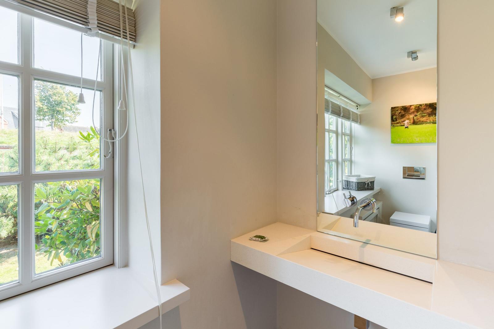 Bathroom with sink, mirror, and window overlooking garden.