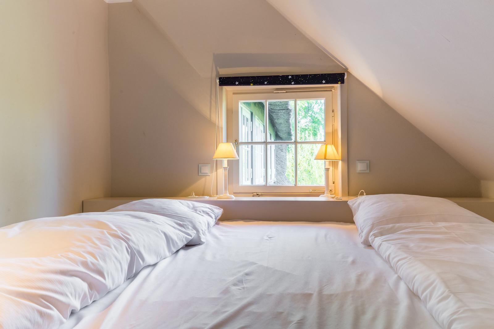Bedroom with sloped ceiling, window, and two bedside tables with lamps.