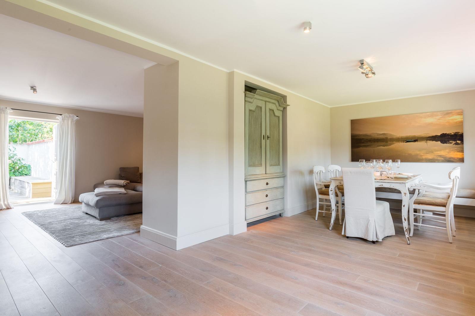 Dining room with table, chairs, and wall art. Passage to living area with sofa and terrace.