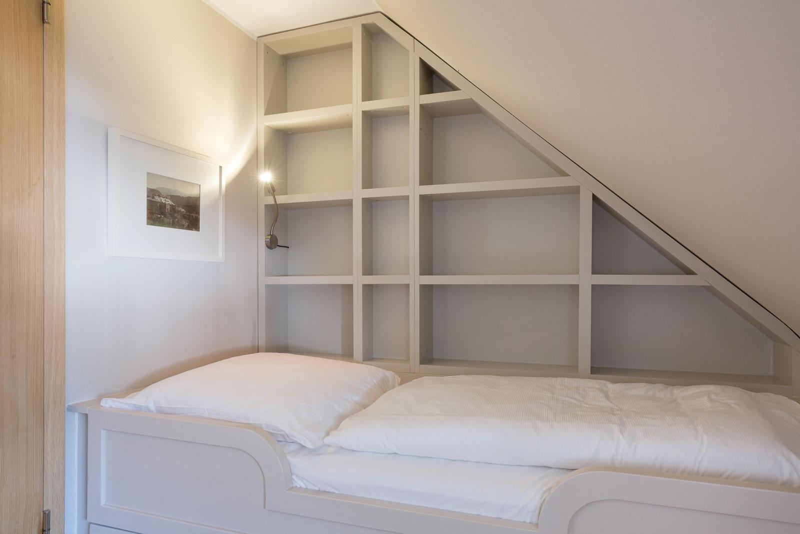 Bedroom with white bed and built-in shelf under sloped ceiling.