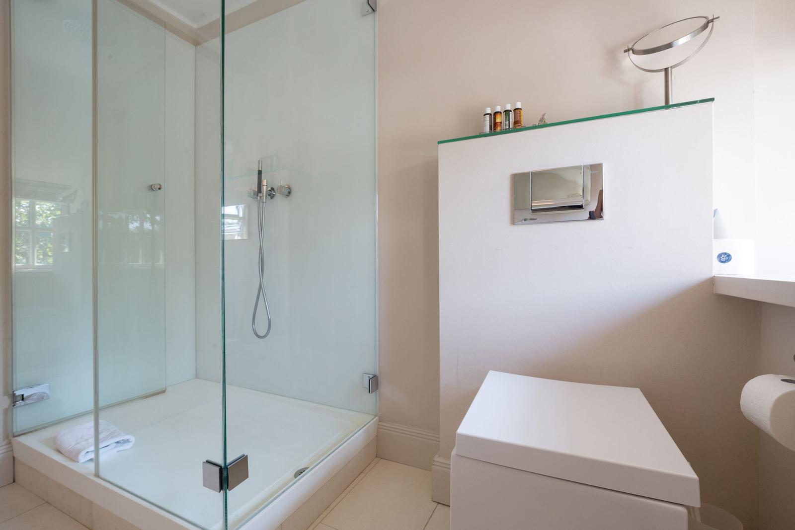 Shower with glass enclosure, toilet, and sink with mirror