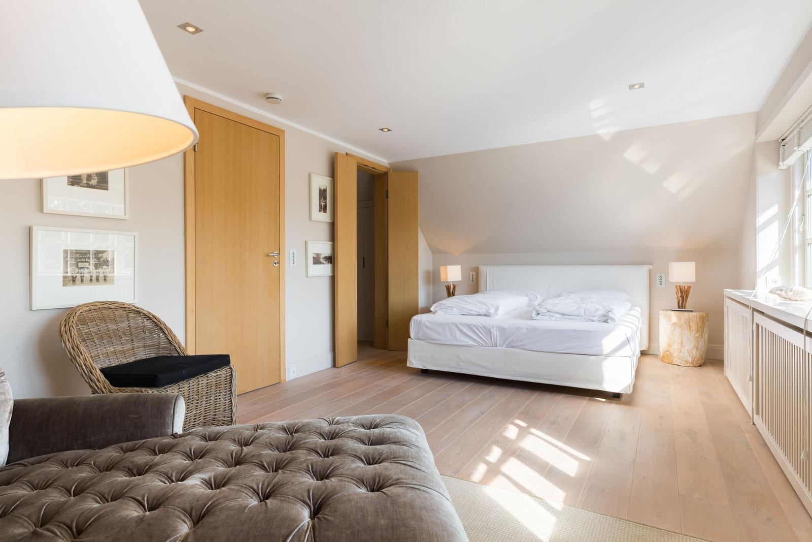 Bedroom with bed, wicker chair, and wooden floor.