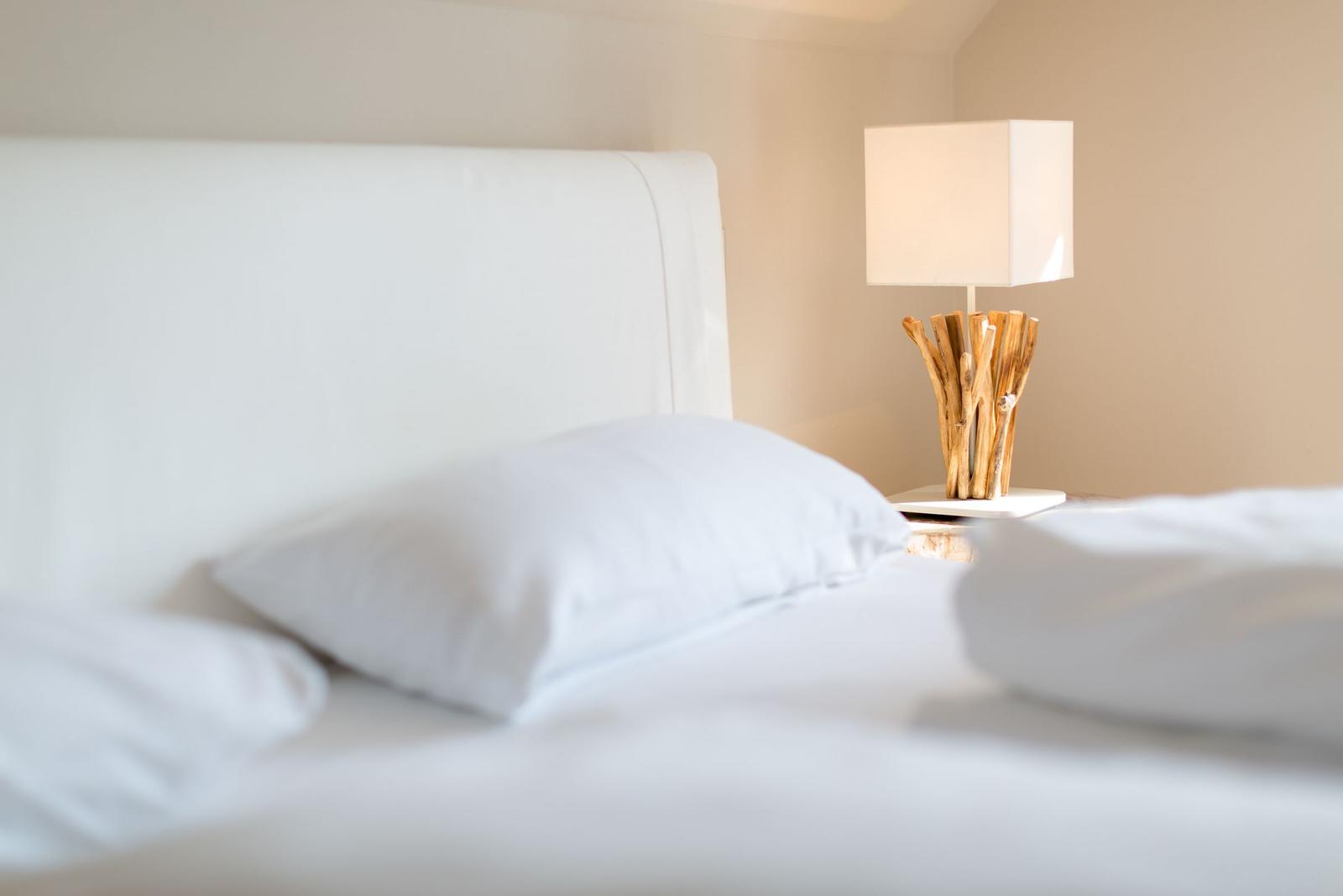 A bed with white linens and a bedside lamp with a wooden base.