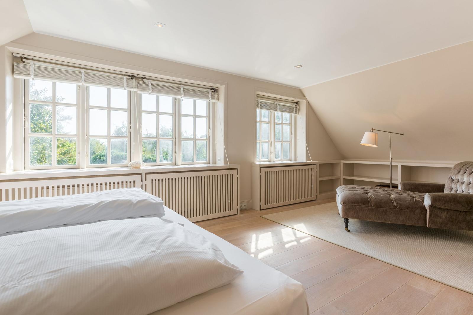 Bedroom with bed, windows, and seating area.