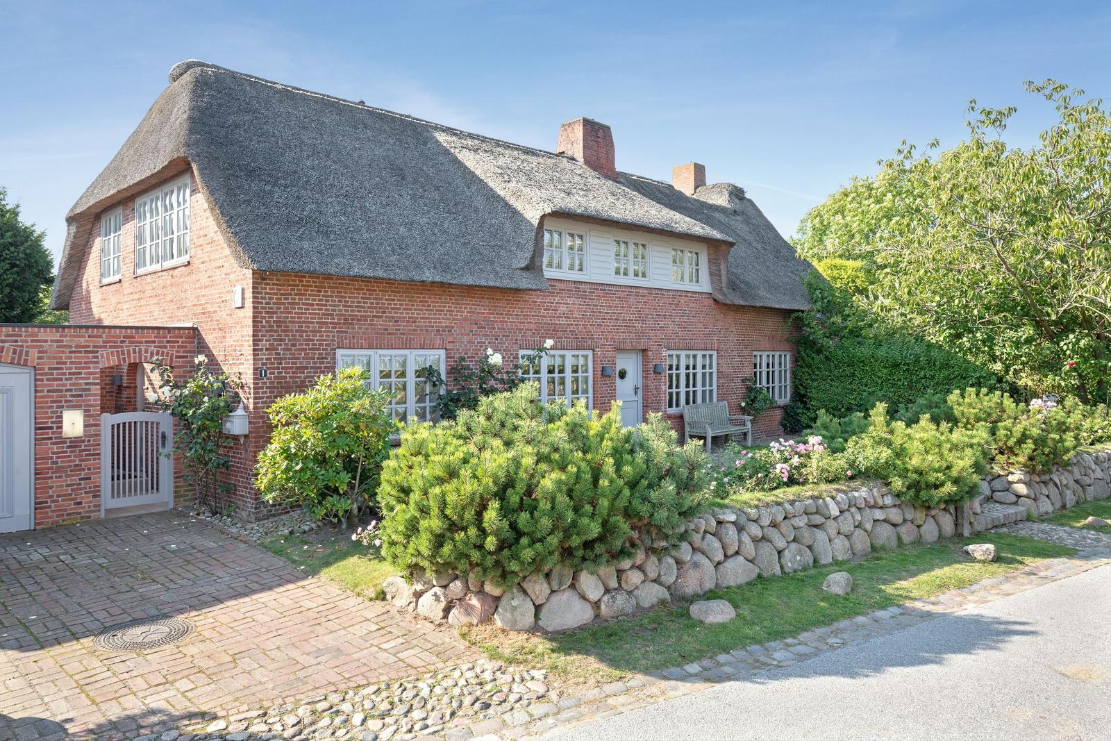Red brick house with thatched roof and well-kept garden.