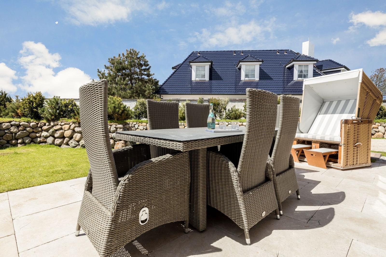Terrasse mit Esstisch und Stühlen, Strandkorb und Haus im Hintergrund.