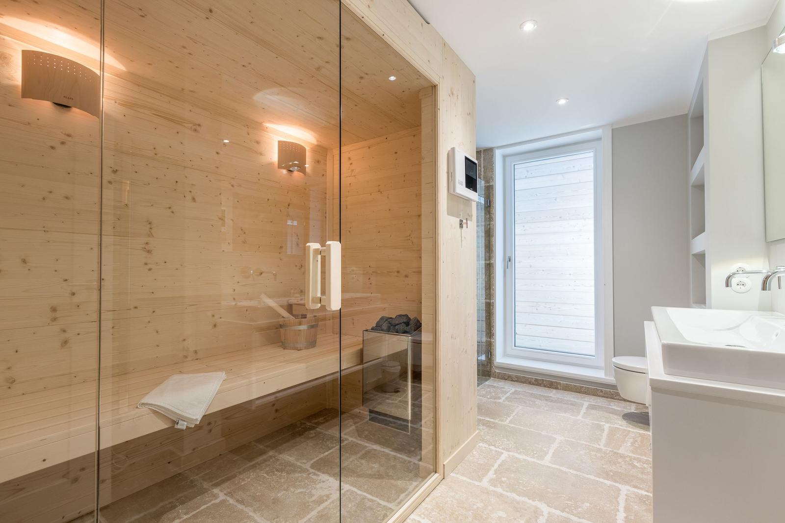 Dusche mit Glaswand, Holzsauna und Waschbecken im Badezimmer.