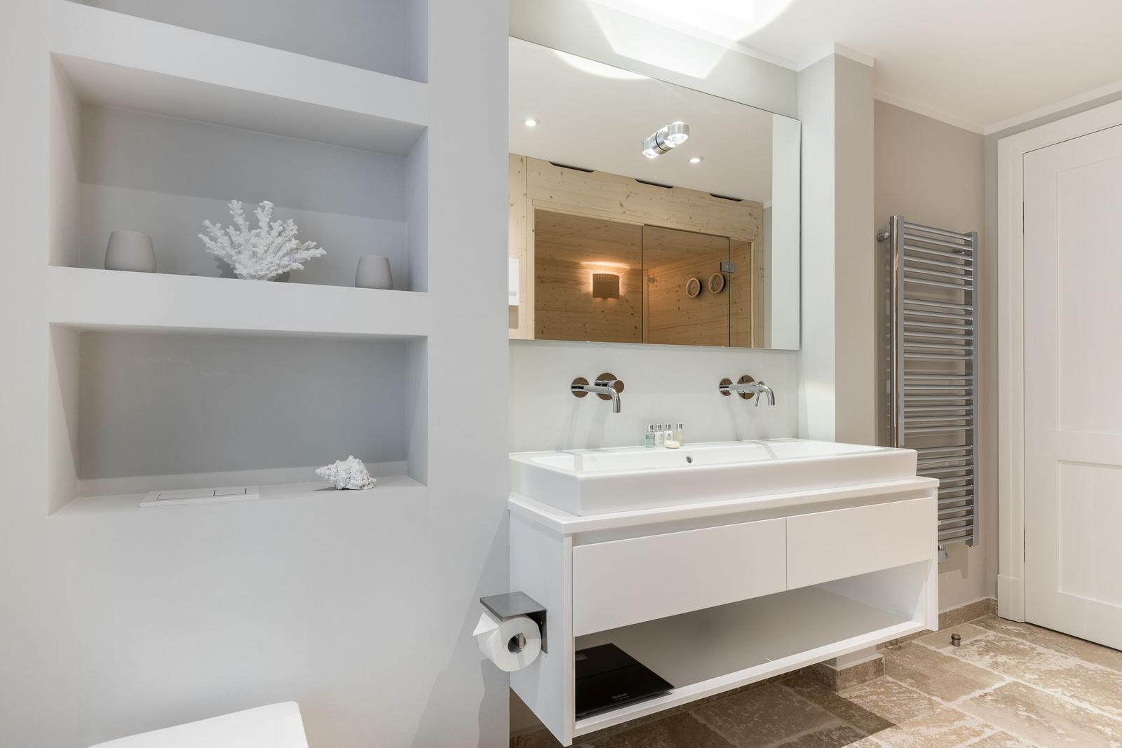 Badezimmer mit Waschtisch, Spiegel und eingelassenen Regalen.