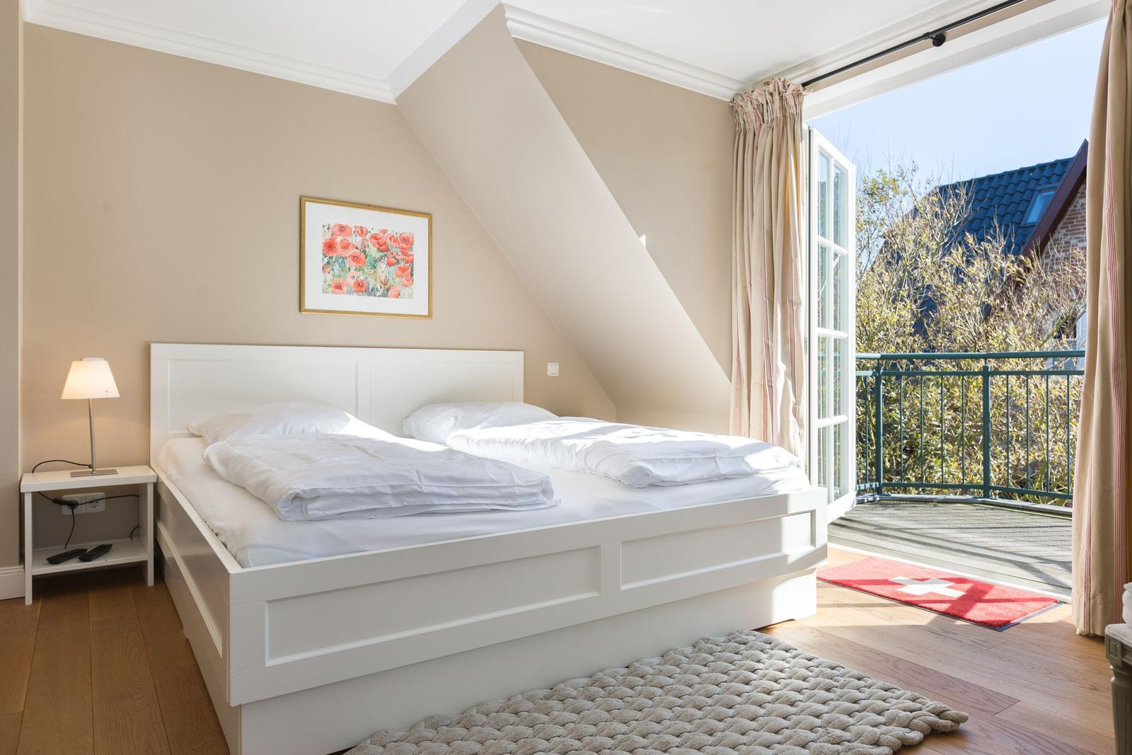 Schlafzimmer mit Dachschrägen, weißem Bett und Balkonzugang.