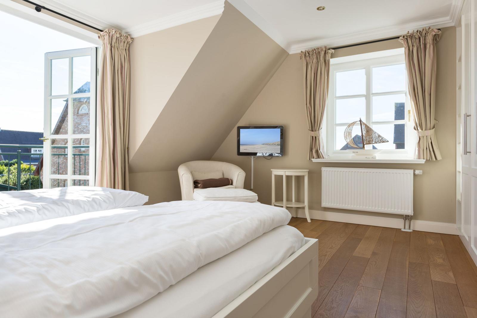 Schlafzimmer mit Dachschrägen, Bett, Sessel, TV und Fenster mit Blick.