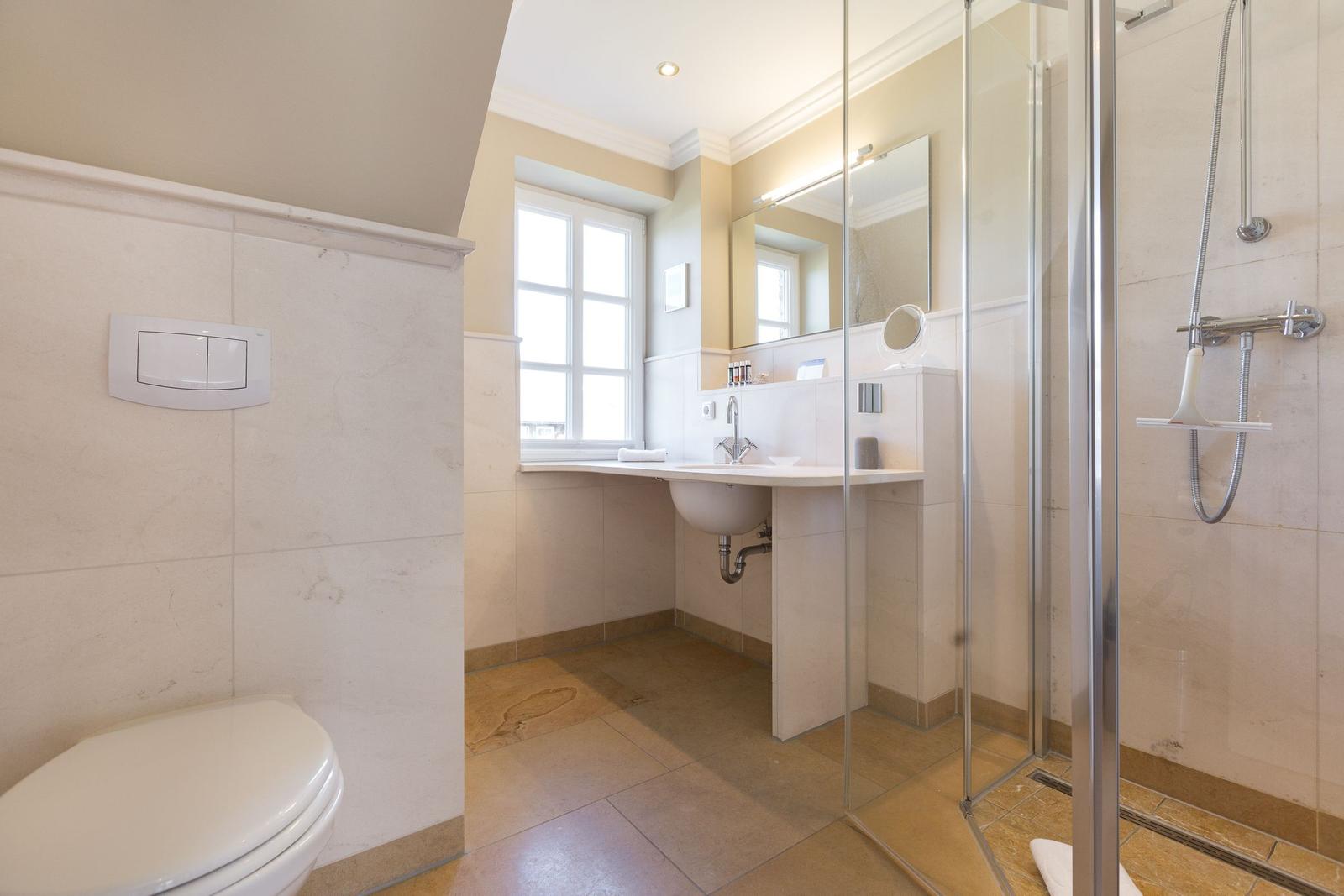Badezimmer mit Dusche, Waschbecken und Toilette. Fenster sorgt für Tageslicht.