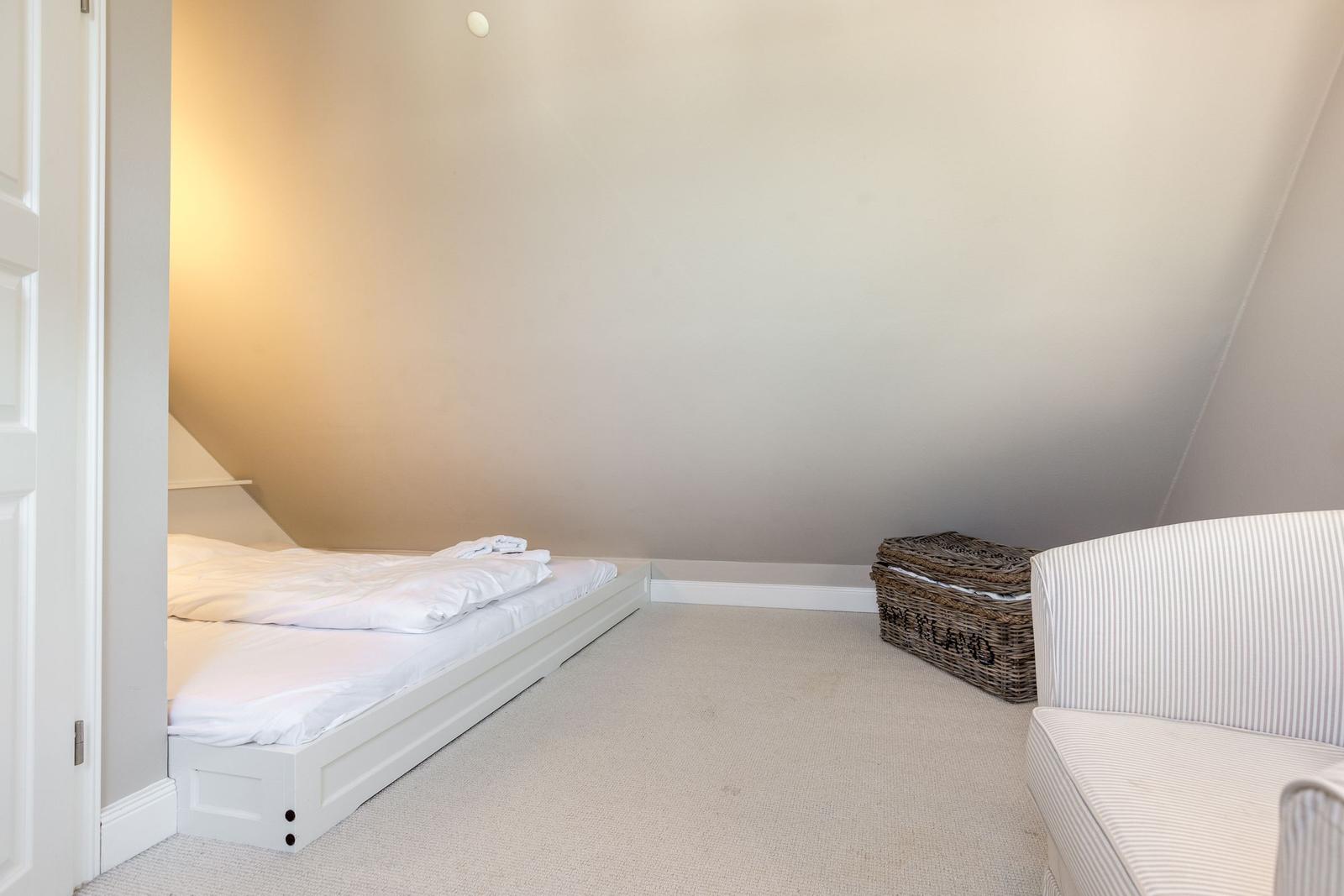 Schlafzimmer mit Dachschrägen, weißem Bett und Streifen-Sofa.