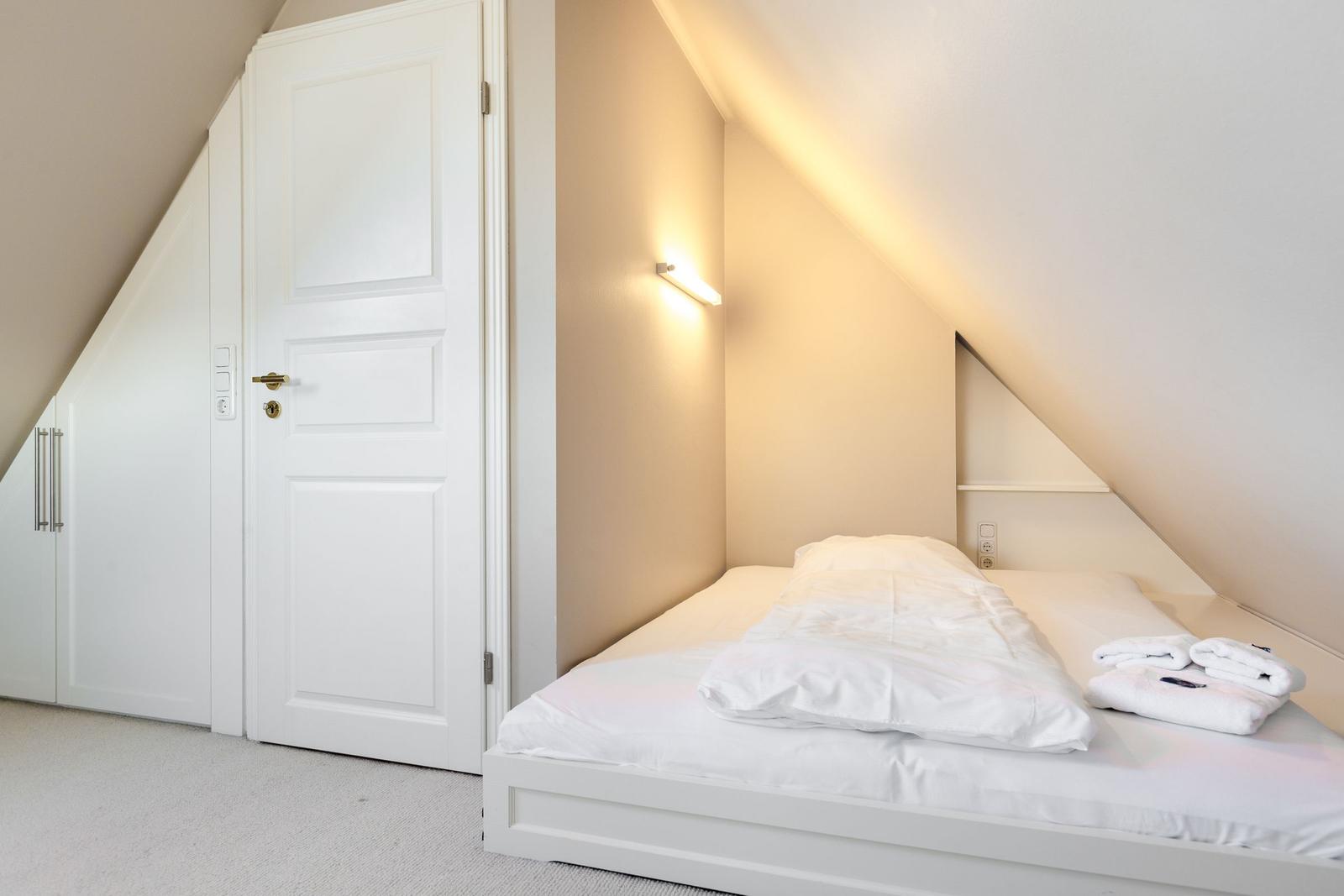 Schlafzimmer mit Dachschrägen, weißem Bett und Kleiderschrank.