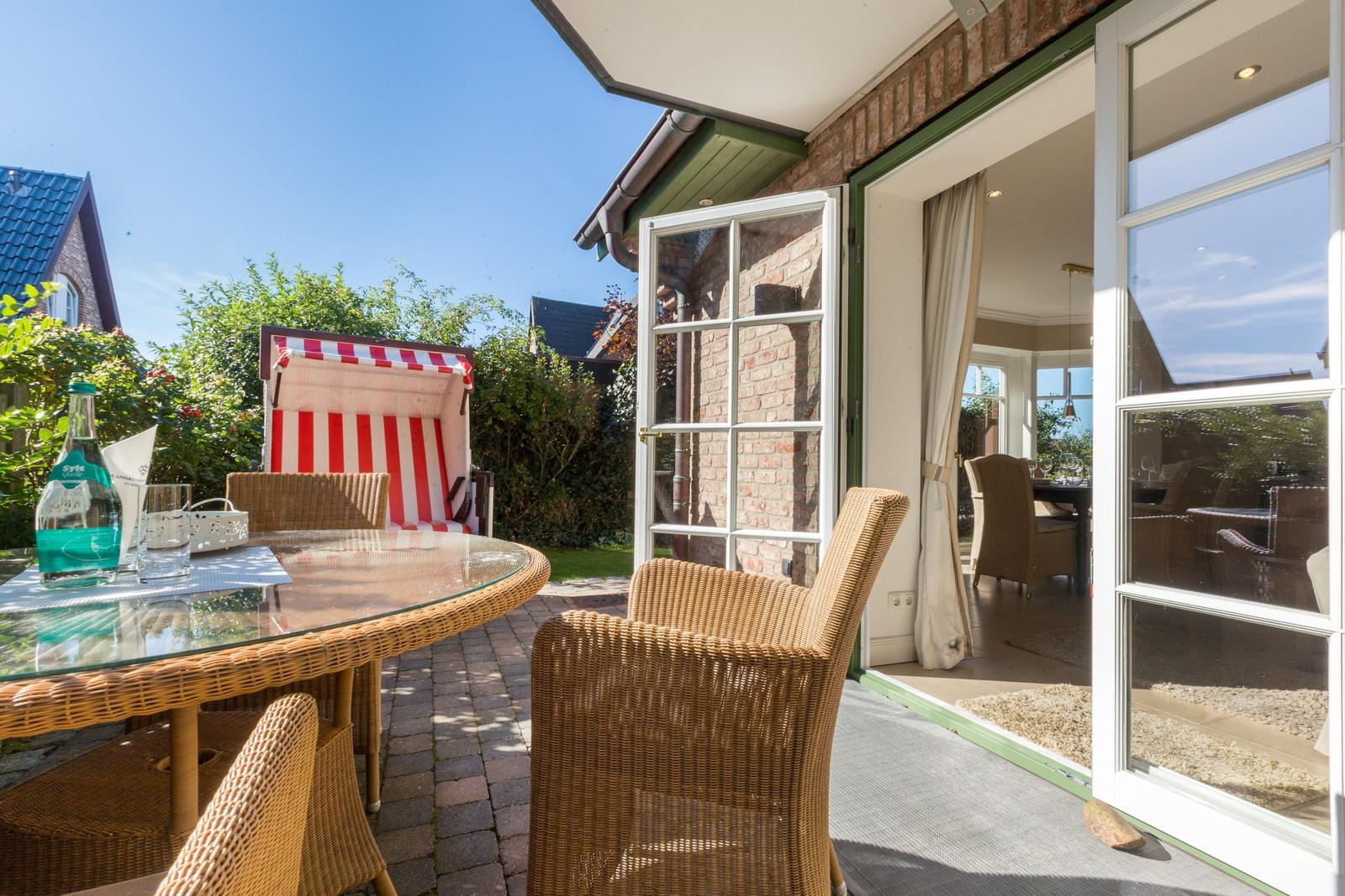 Terrasse mit Esstisch, Stühlen und Strandkorb. Durchgang ins Haus.