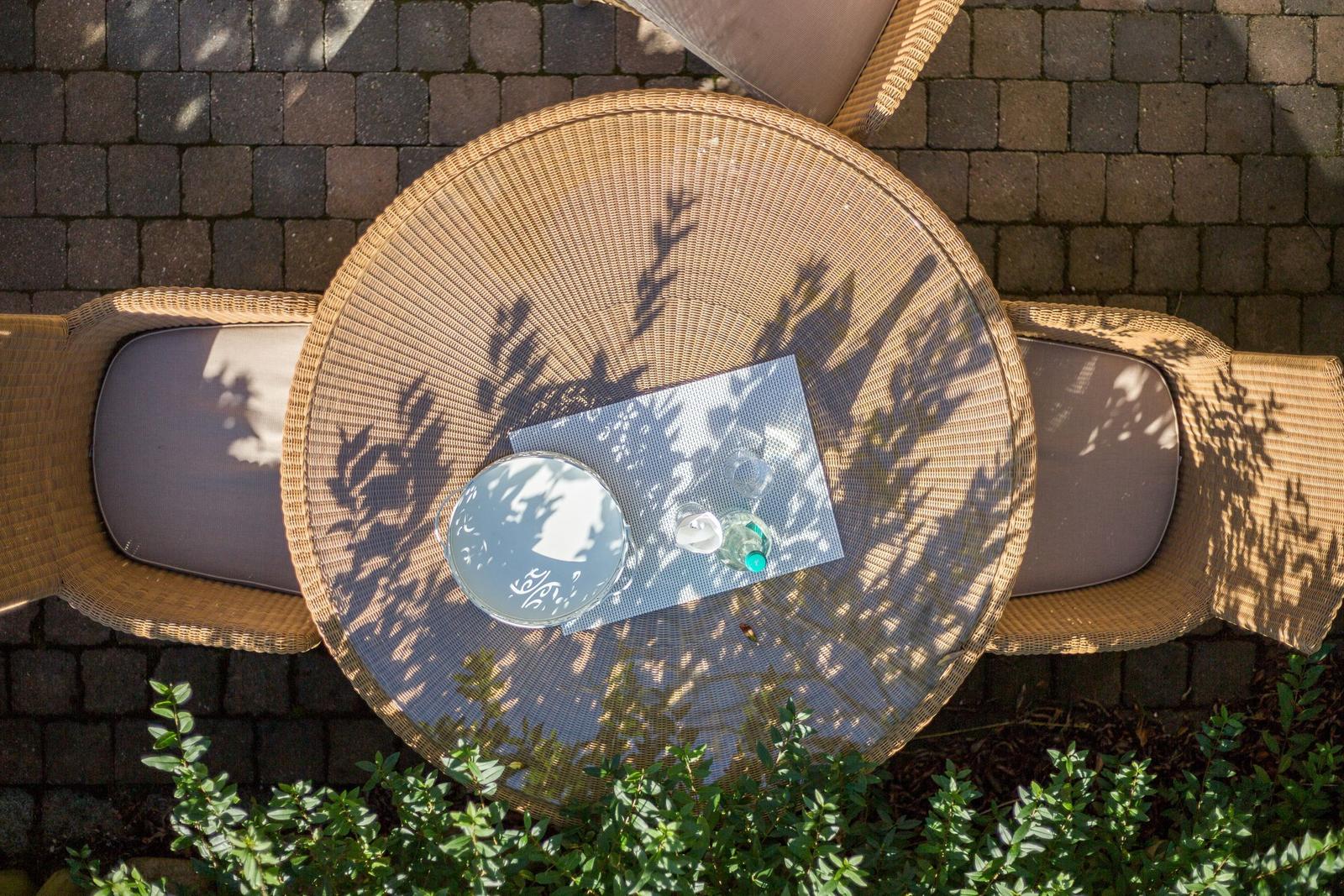 Runder Wicker-Tisch mit drei Stühlen und Getränken auf Steinplatten.