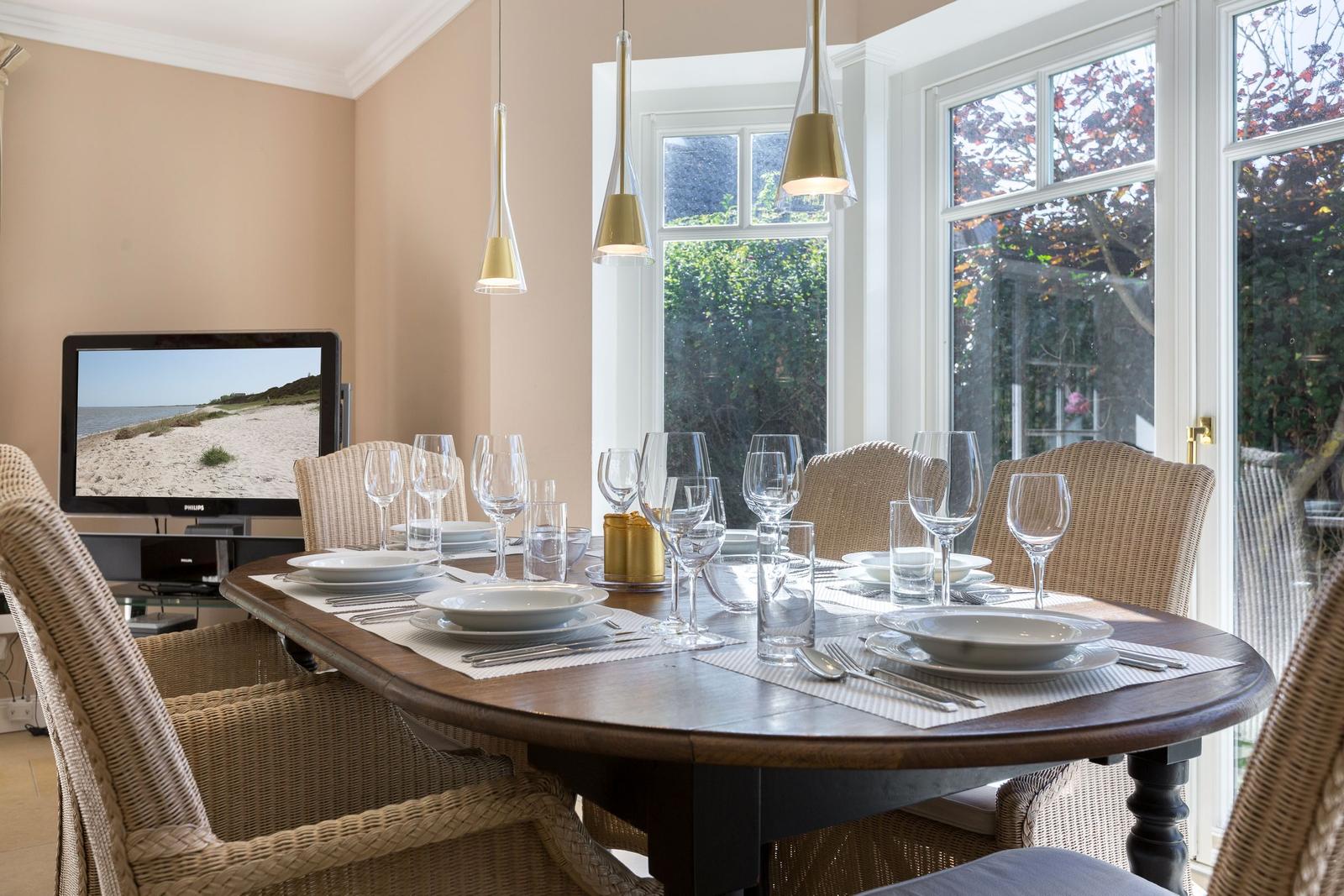Esszimmer mit gedecktem Tisch, wickerstühlen und Fensterblick.