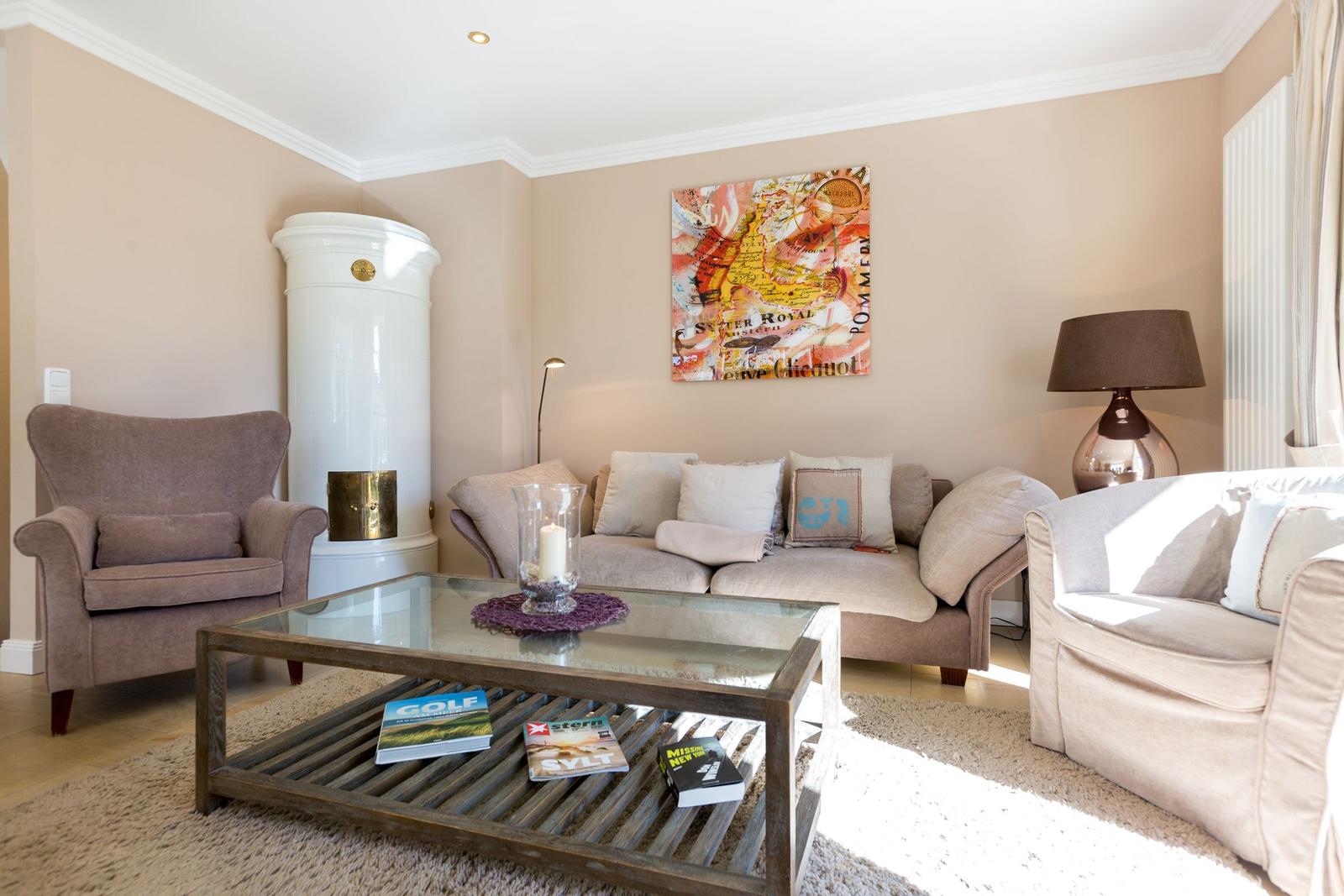 Wohnzimmer mit Sofa, Sessel und Glas-Tisch. Weiße Kaminwand und Wandbild.