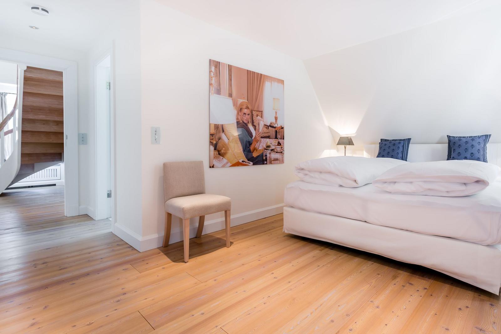 Bedroom with bed, chair, and wall art. Wooden floor and white walls.