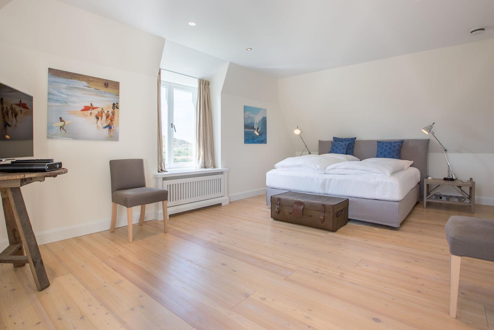 Bedroom with bed, window, wall art, and wooden floor.