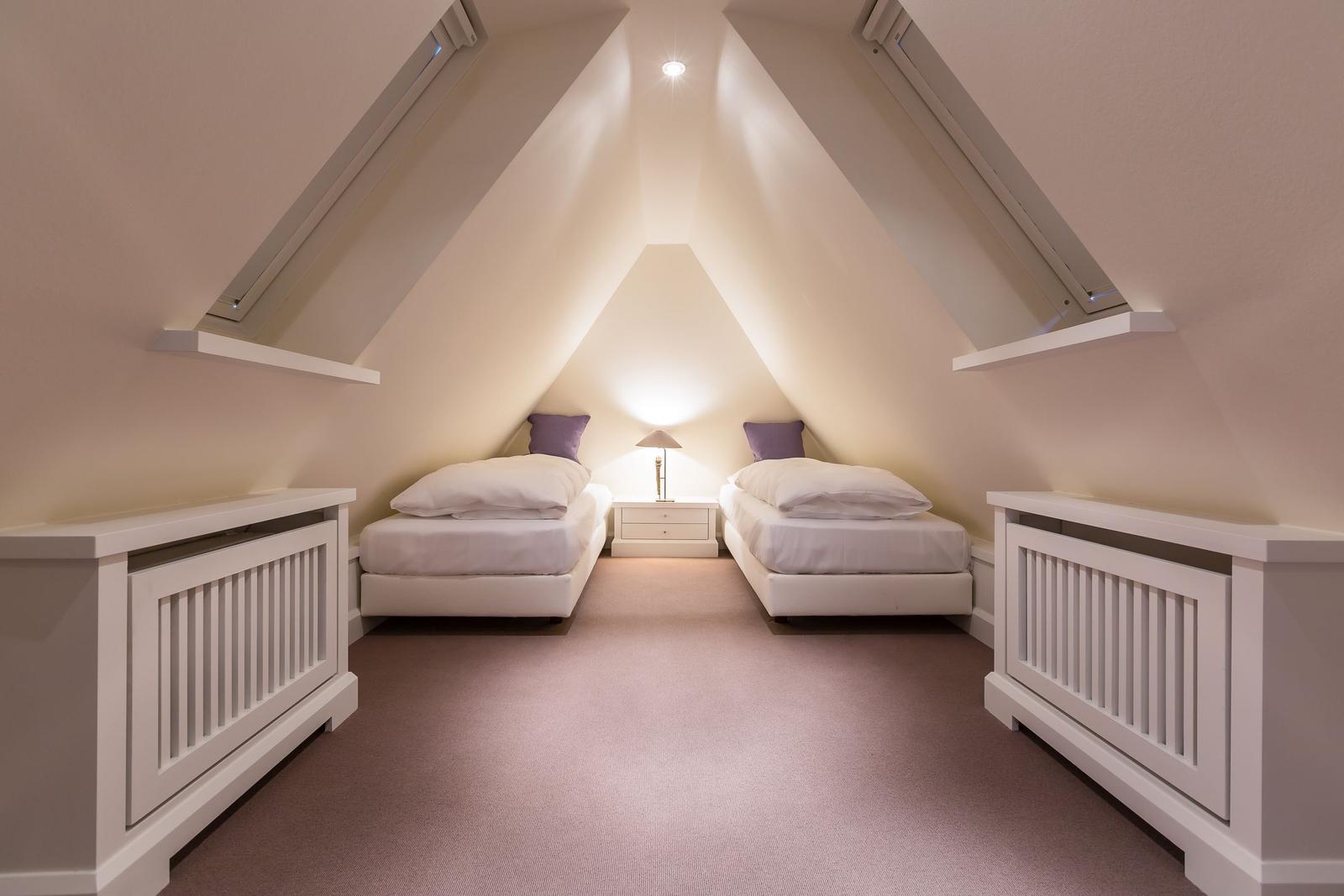 Two single beds under sloped ceilings with nightstand and lamp.