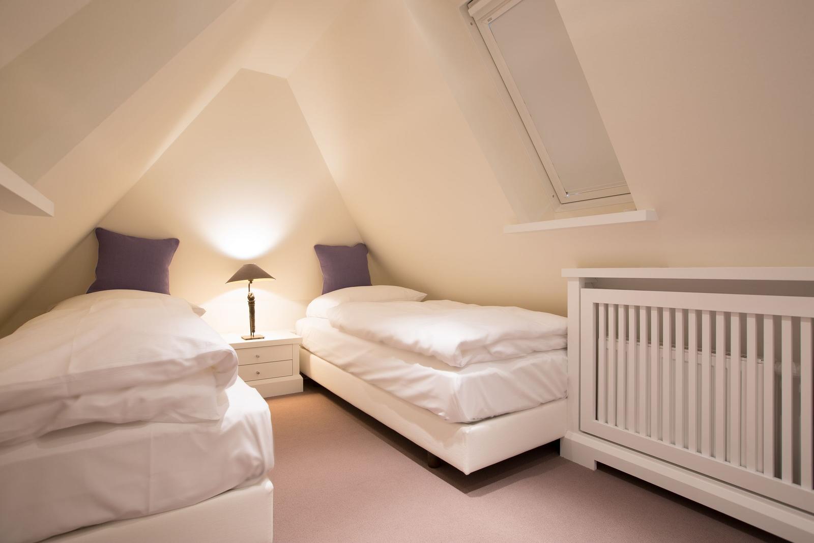 Two beds and a crib in an attic room with skylight.