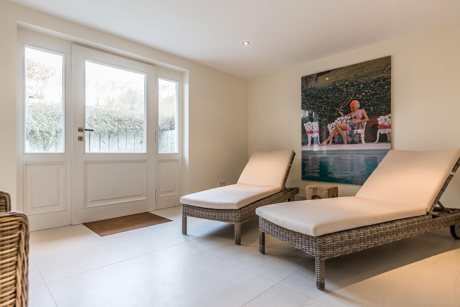 Two lounge chairs are positioned before a glass door. A large picture hangs on the wall.