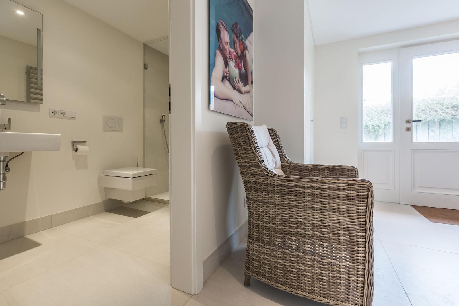 Hallway with chair and view into bathroom. Wall art and door with glass panel.