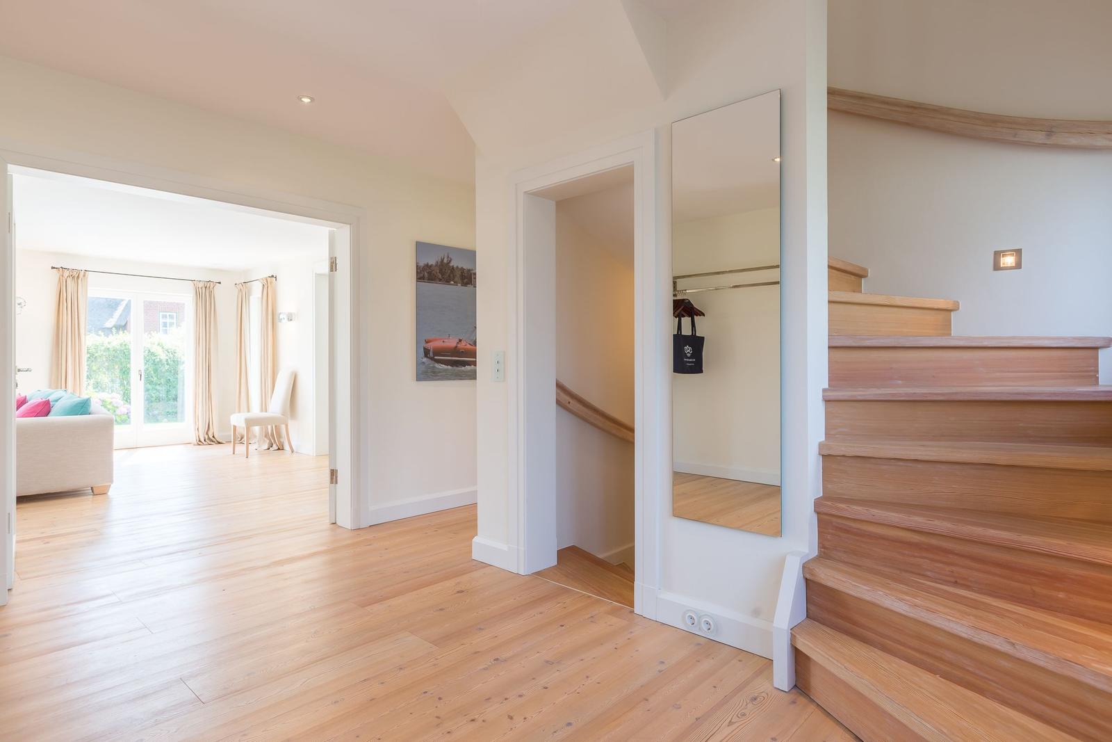 House with wooden staircase, mirror, and view into living area with sofa and window.